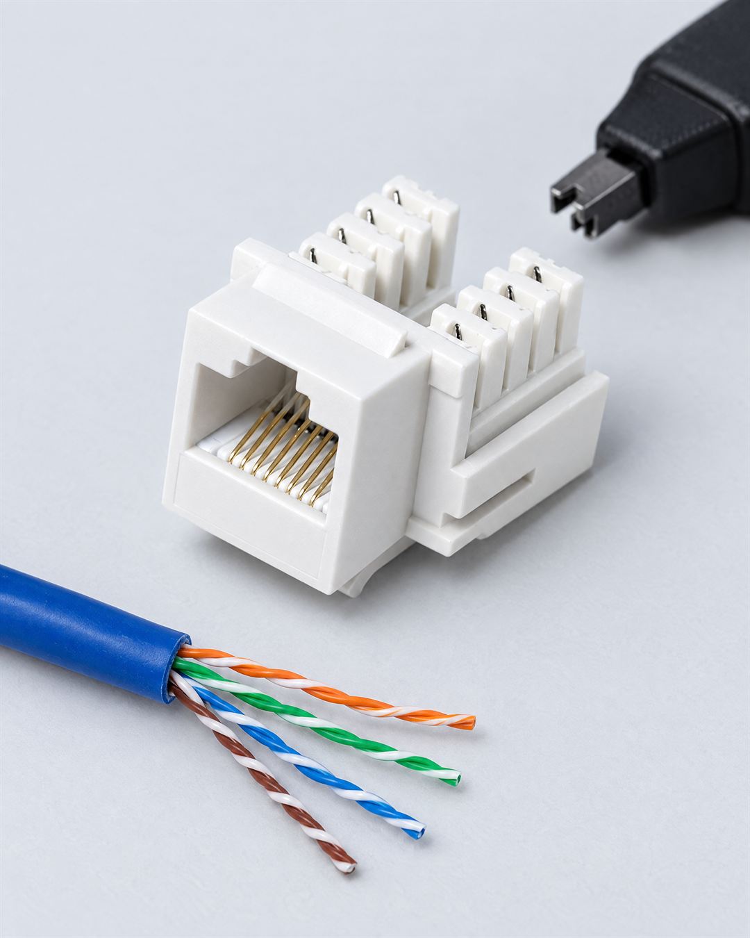 Un conector keystone Cat6 blanco junto a un cable Cat6 azul pelado, con sus cuatro pares trenzados, y una herramienta de impacto para ponchar.